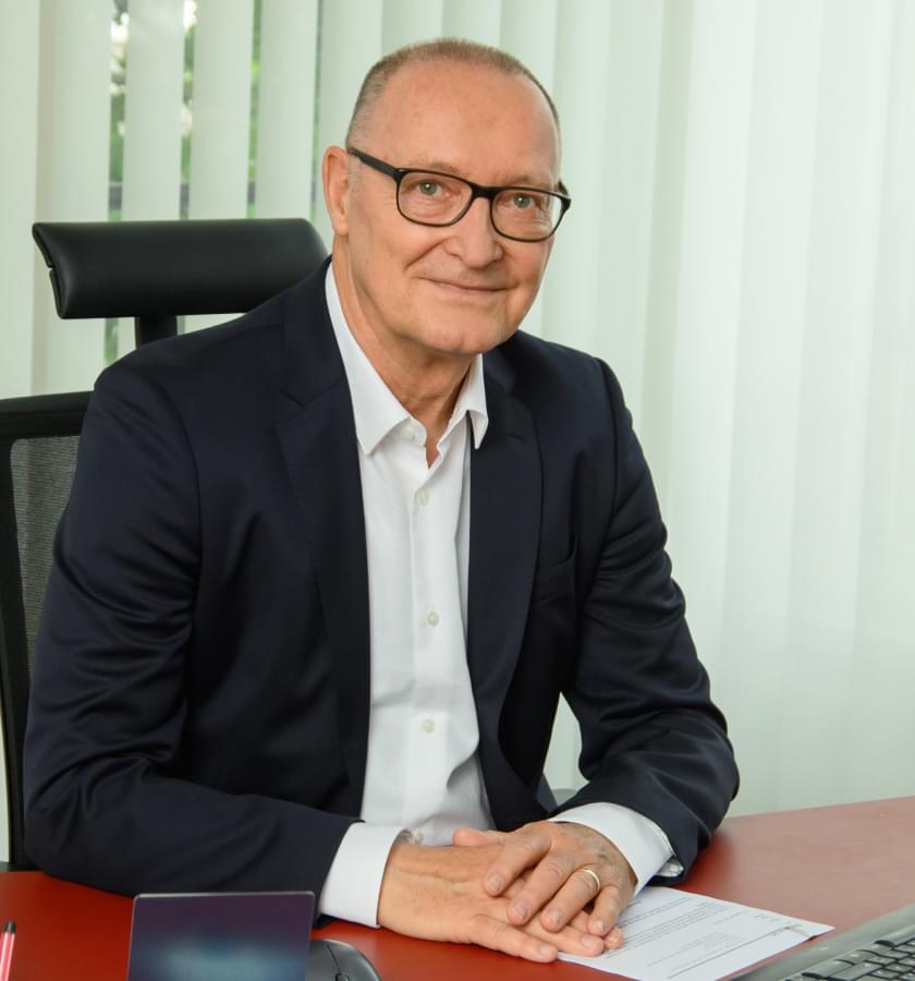 Foto von Herrn Prof. Dr. Bertram Schmitt, Schlichter der Schlichtungsstelle. Ein älterer Herr mit Brille, der einen schwarzen Anzug und ein weißes Hemd trät, sitzt an einem Schreibtisch.