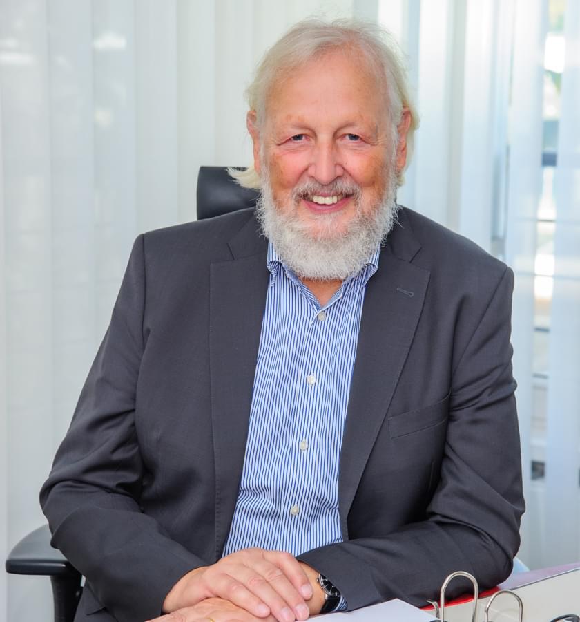 Foto von Martin Dreßler, ein älterer Herr mit weißen Haaren und weißem Bart trägt einen grauen Anzug und ein blau-weiß gestreiftes Hemd