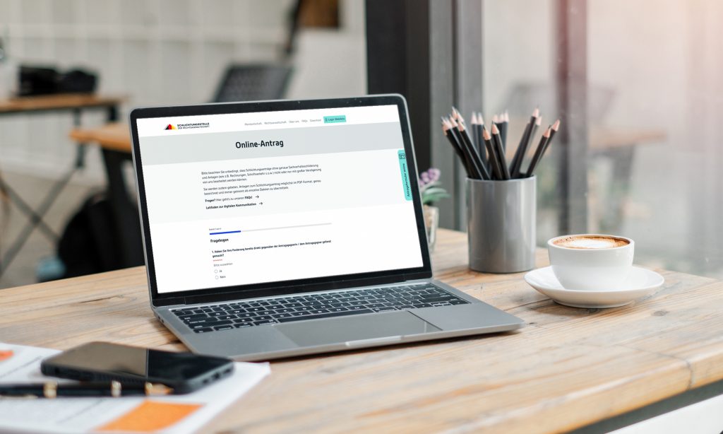 Foto eines Laptops der auf einem Schreibtisch steht. Auf dem Laptop sieht man die geöffnete Seite des Online-Antrags der Schlichtungsstelle.